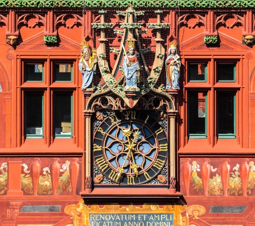 Die Uhr in der Fassade des Rathauses. Darüber drei Figuren, in der Mitte Justitia, links etwas zurückversetzt Kaiser Heinrich II, auf der rechten Seite Heinrichs Gattin Kunigunde.